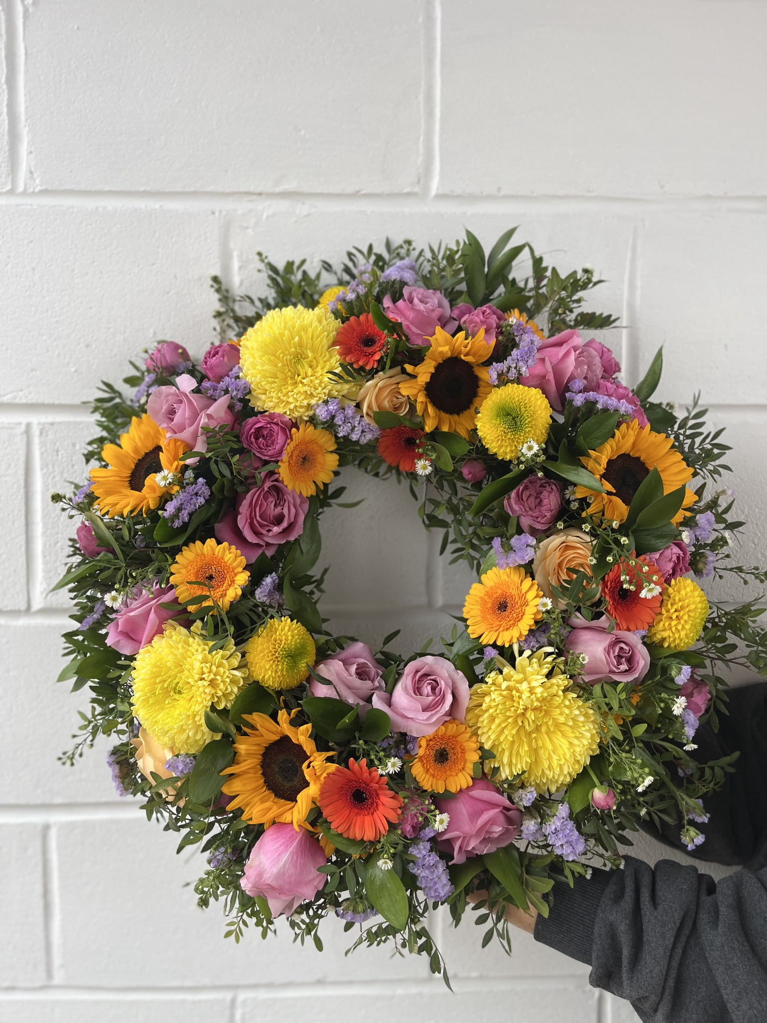 Colourful circular funeral wreath with sunflowers, pink roses and yellow chrysanthemums by Extra Fleur